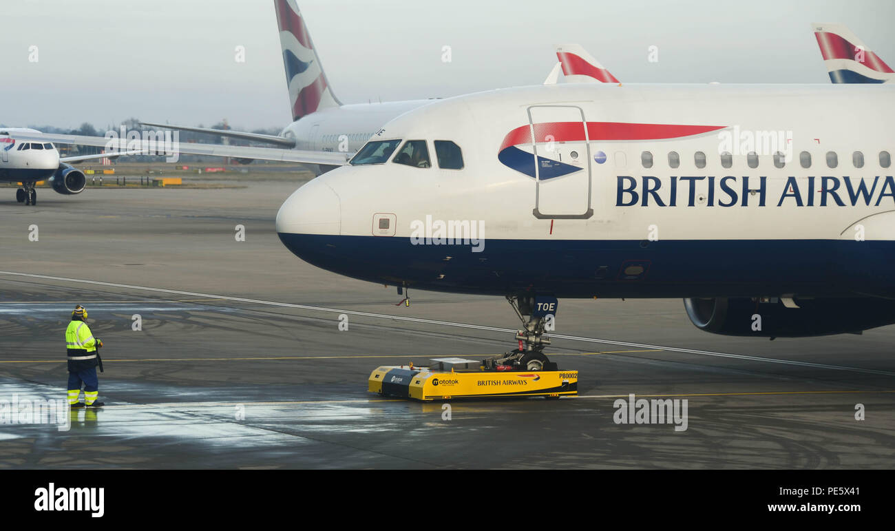 Airport worker operating a remote controlled tug at London Heathrow Airport to push back a departing British Airways Airbus A320 Stock Photo