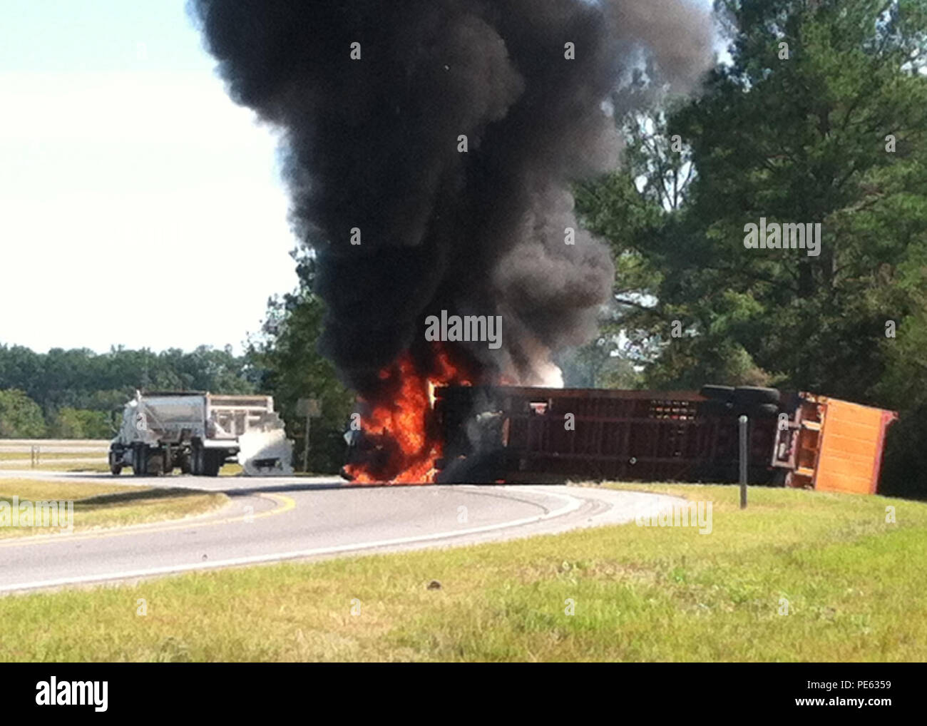A semi-truck is engulfed in flames after an accident between the semi and a disabled vehicle caused it to flip. Four Coast Guardsmen, with Coast Guard Sector Mobile, witnessed the accident, called 911 and quickly responded by pulling the unconscious truck driver from the semi-truck cab before it was engulfed in flames, and rendered first aid until local emergency medical services arrived on-scene. (U.S. Coast Guard photo courtesy of Coast Guard Sector Mobile) Stock Photo