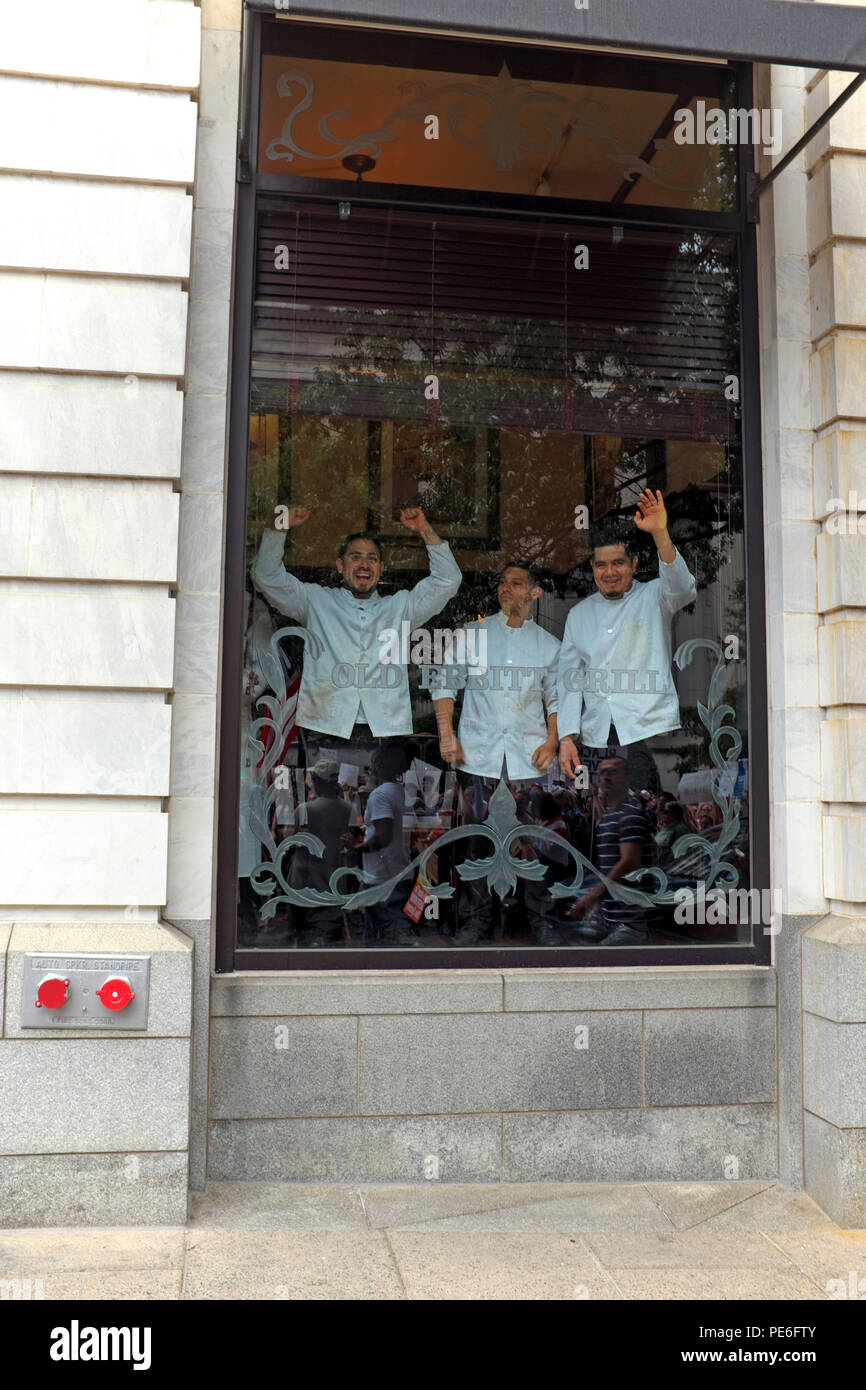 Washington D.C., USA.  12th August, 2018. Male servers inside the Old Ebbitt Grill on 15th Street NW in Washington D.C. look out the front window and cheer as the alt-right counterprotest march makes its way past the restaurant.  One can see marchers in the reflection of the glass.  The servers are obviously jubilant at what they are witnessing. Credit: Mark Kanning/Alamy Live News. Stock Photo