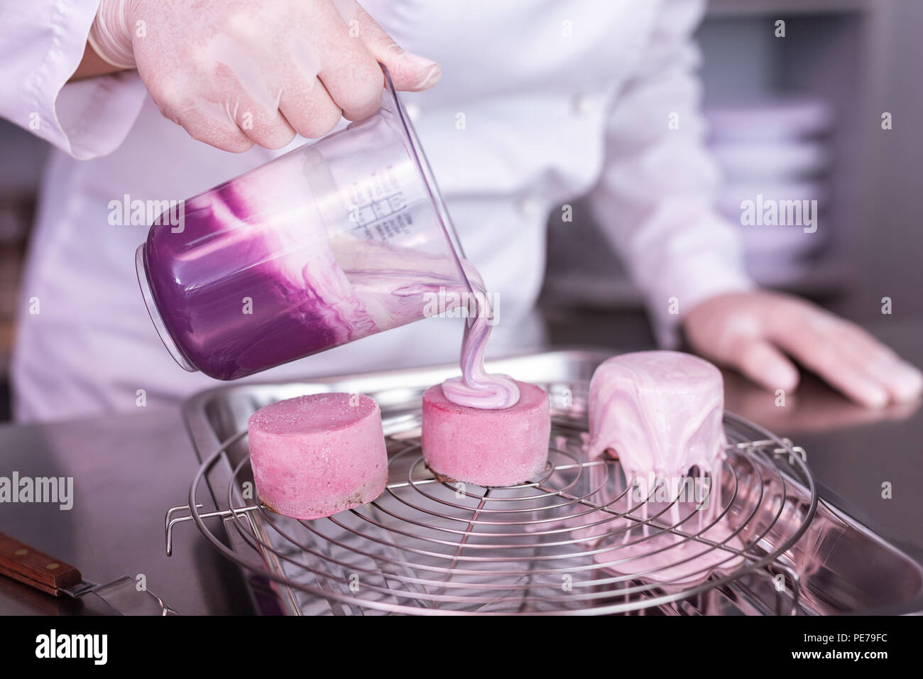 Experienced baker pouring nice violet mirror icing on little cakes Stock Photo
