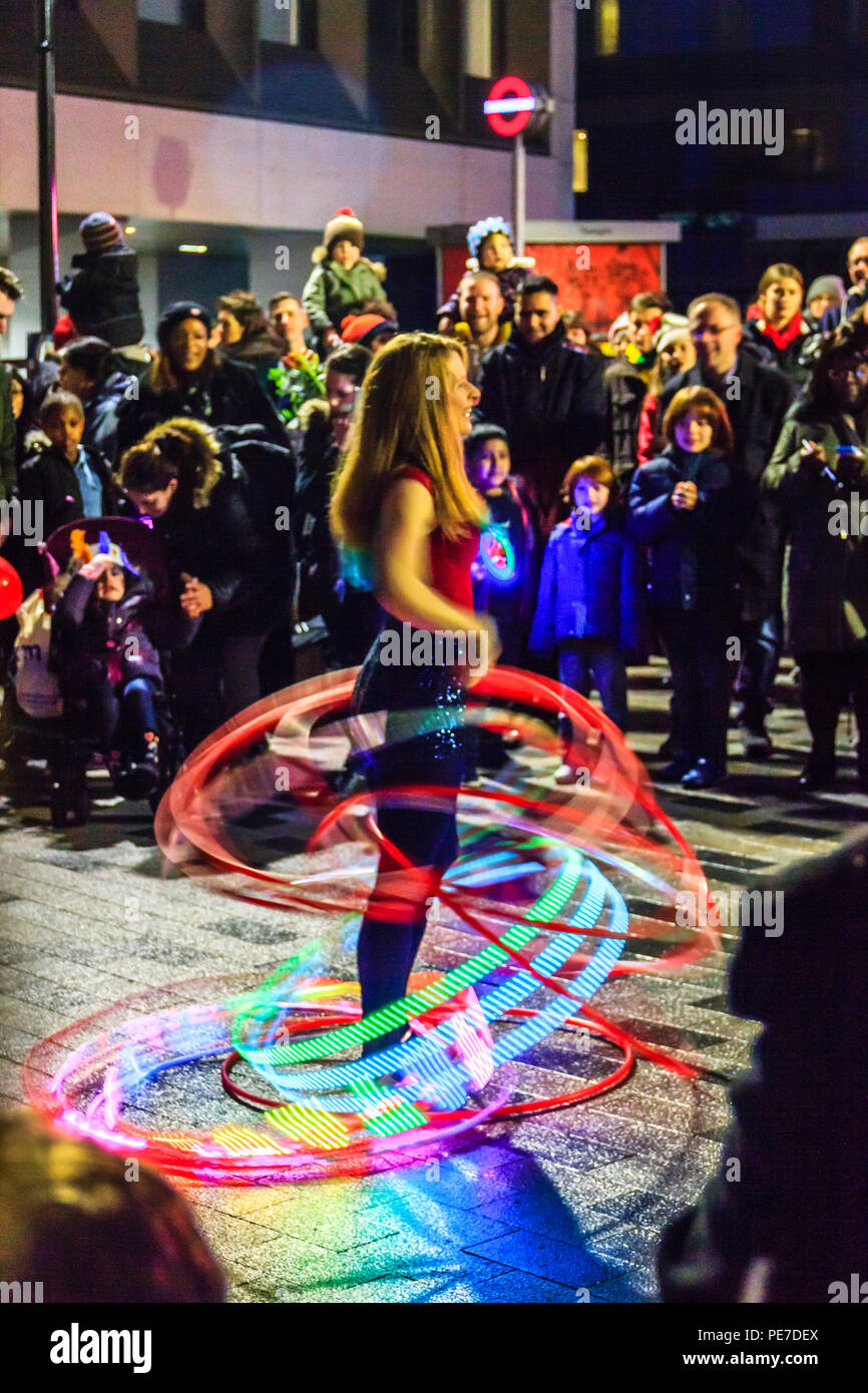 A female hula hoop artist giving a night-time demonstration in Navigator Square, Archway, London, UK, using multiple illuminated hoops Stock Photo