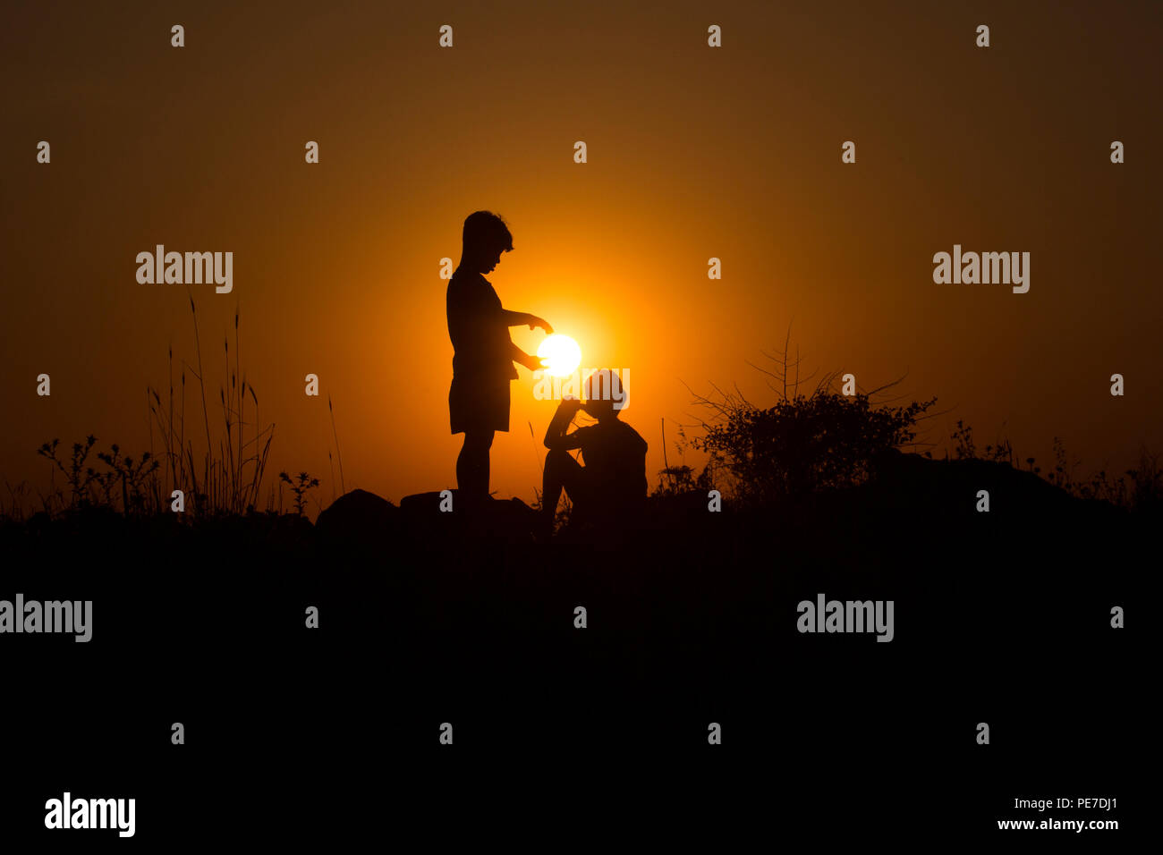 A young boy is offering the setting sun to the young girl next to him Stock Photo