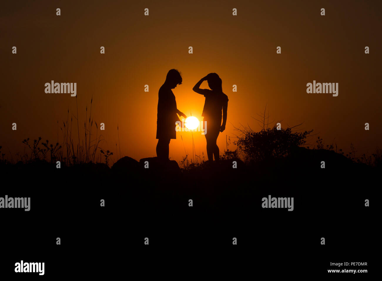 A young boy is offering the setting sun to the young girl next to him Stock Photo