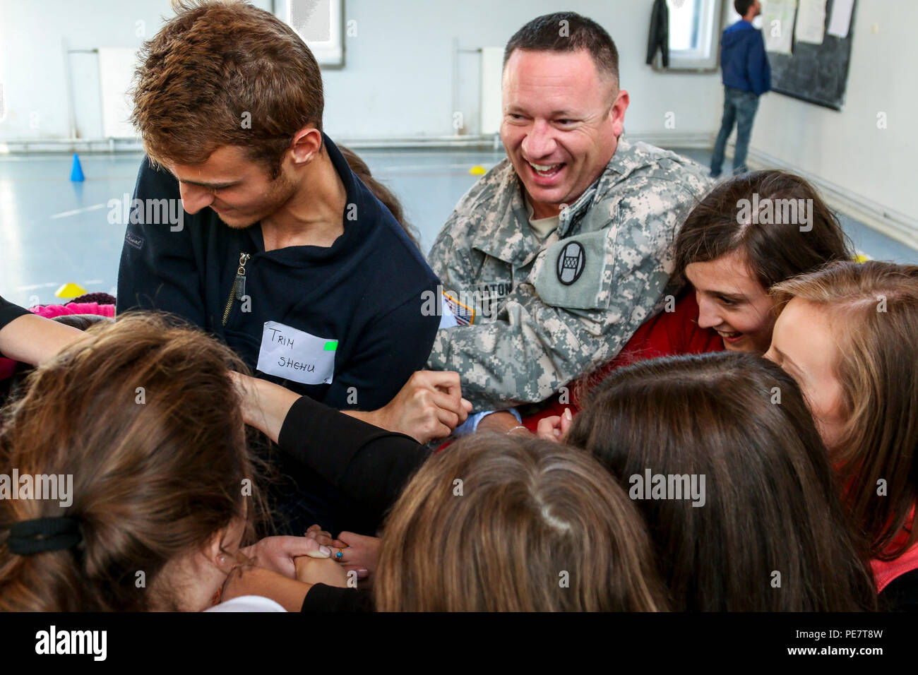 Capt. Jonathan Laton, a North Carolina National Guard Soldier deployed to Kosovo with the 30th Armored Brigade Combat Team headquarters, laughs alongside a group of students while leading them in a game called The Human Knot, during an Oct. 17, 2015, Violence Free Future youth tolerance event in Kacanik, Kosovo. During the game, the participants to used teamwork and communication skills to untangle themselves without letting go of each other’s hands. Laton and several other members of Multinational Battle Group-East volunteered their free time to lead this and other games used to simulate real Stock Photo