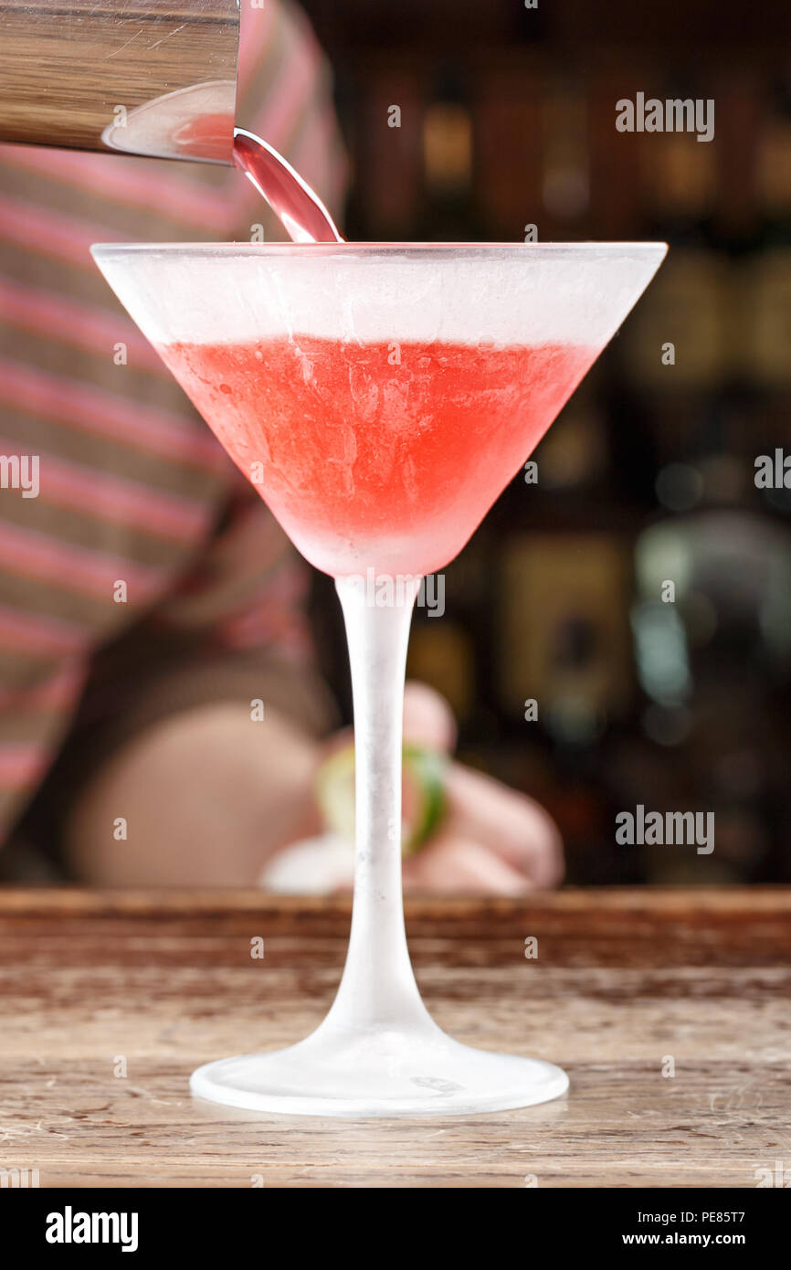 A cosmopolitan cocktail is poured into a glass from a shaker. The