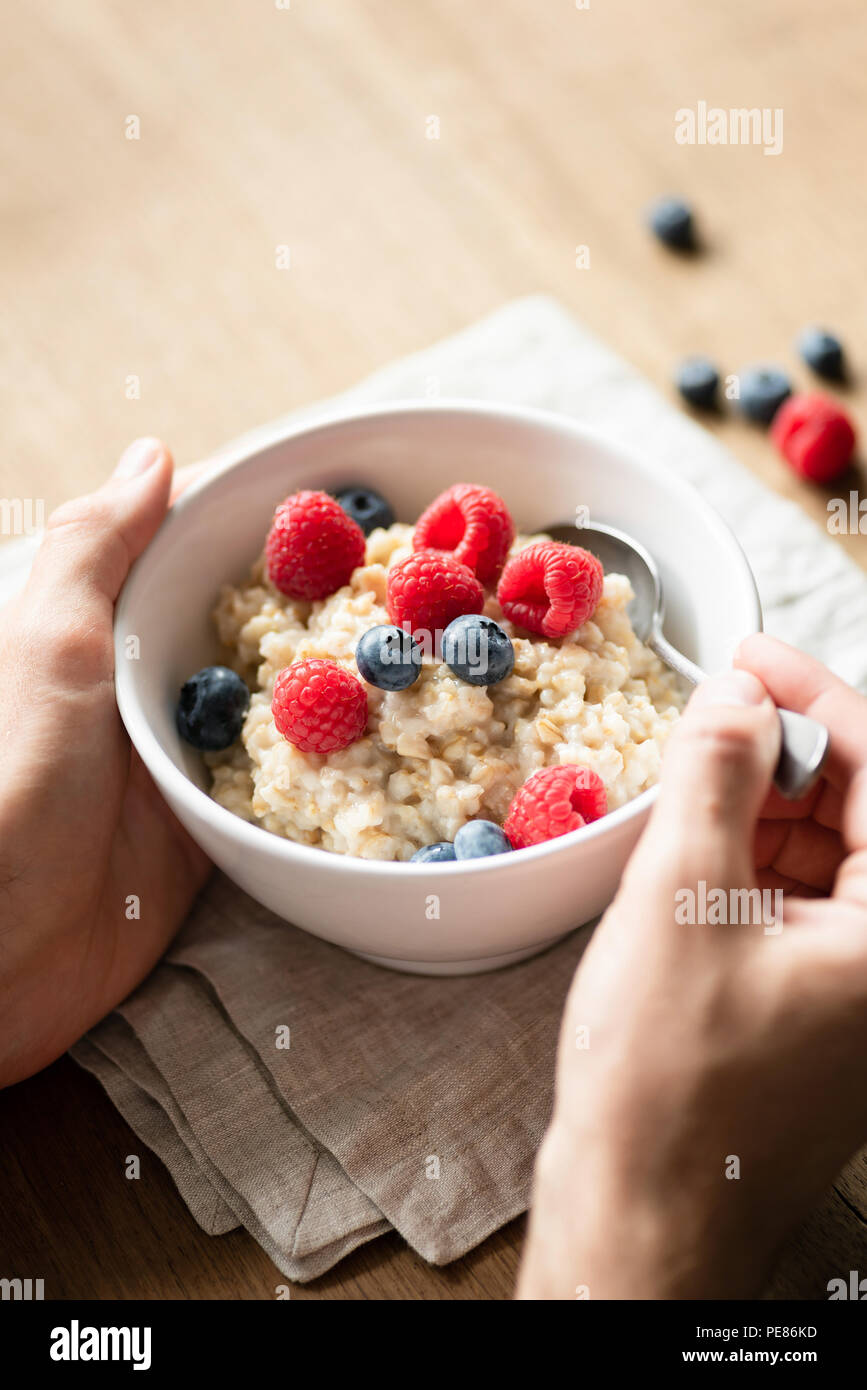 Oatmeal porridge with berries in hands. Person eating healthy breakfast Stock Photo