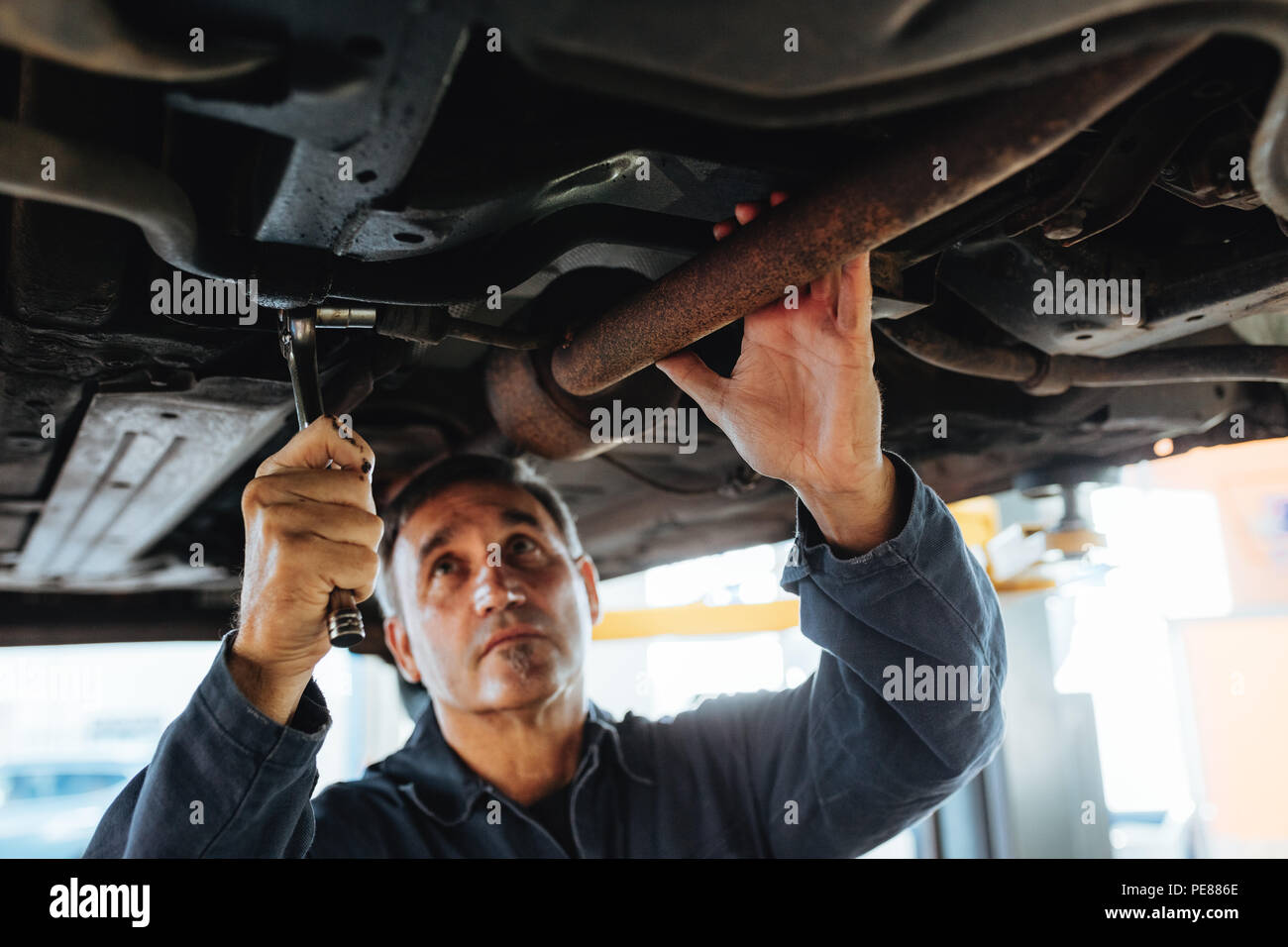 Man tightening a silencer pipe with wrench spanner in auto garage