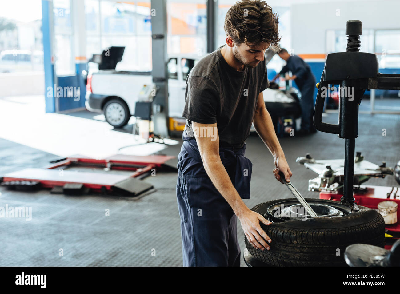 Repairman replacing tire on wheel in workshop. Mechanic changing car tire in service station. Stock Photo