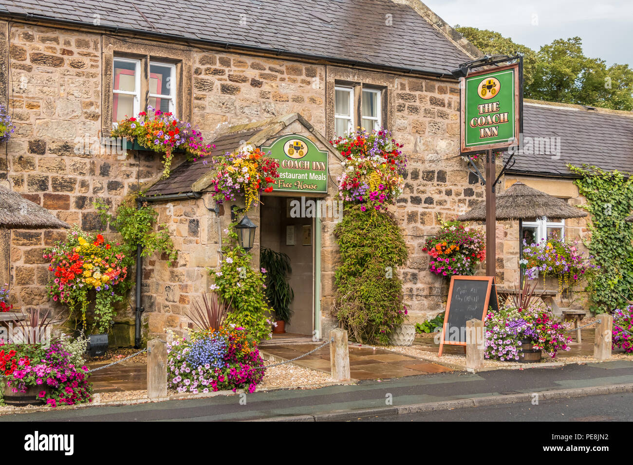 Traditional English country pub, The Coach Inn, Lesbury, Northumberland with a colourful display of flowering hanging baskets and tubs Stock Photo