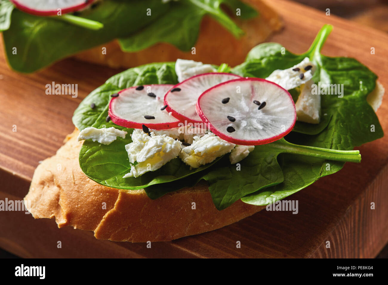 Light healthy sandwiches with bread toasts, soft cheese and freshly gathered organic radishes, spinach on a wooden board. Stock Photo