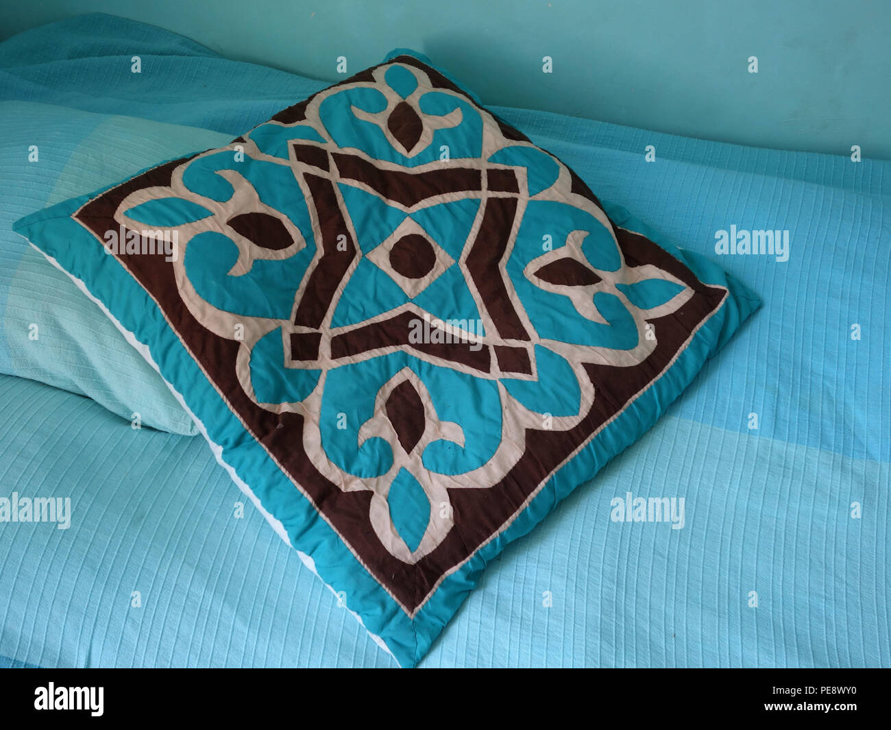 Patterned egyptian styled cushion in turquoise blue colour on a blue bed cover in large French house Stock Photo