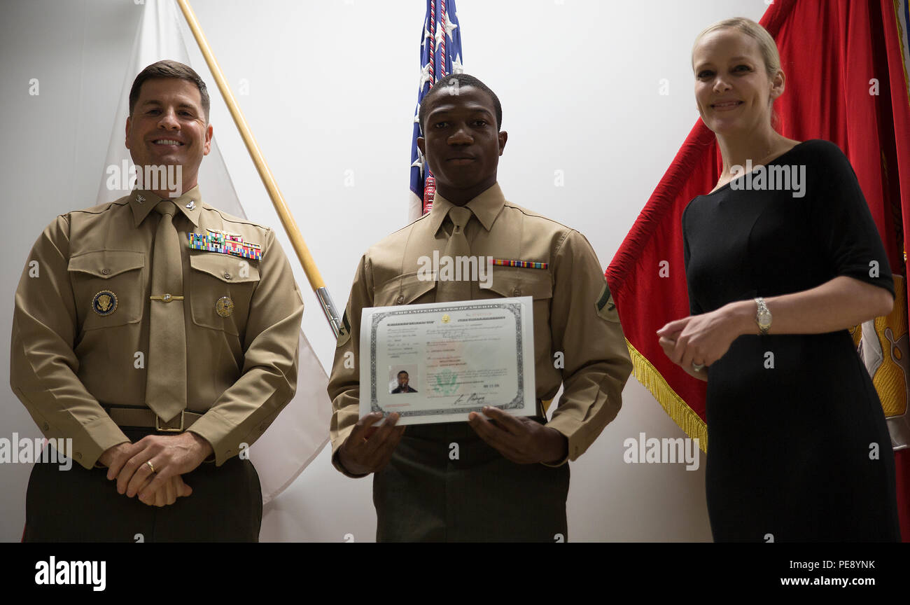 Lance Cpl. Benjay Williams, middle, receives his certificate of naturalization from Col. Robert V. Boucher, left, station commanding officer and Kim Shipley, right, special assistant at International Operations of United States Citizens and Immigration Services at the Building One auditorium at Marine Corps Air Station Iwakuni, Japan, Nov. 5, 2015. Williams volunteered to read the Pledge of Allegiance before recipients received their naturalization certificates. (U.S. Marine Corps photo by Lance Cpl. Aaron Henson/Released) Stock Photo