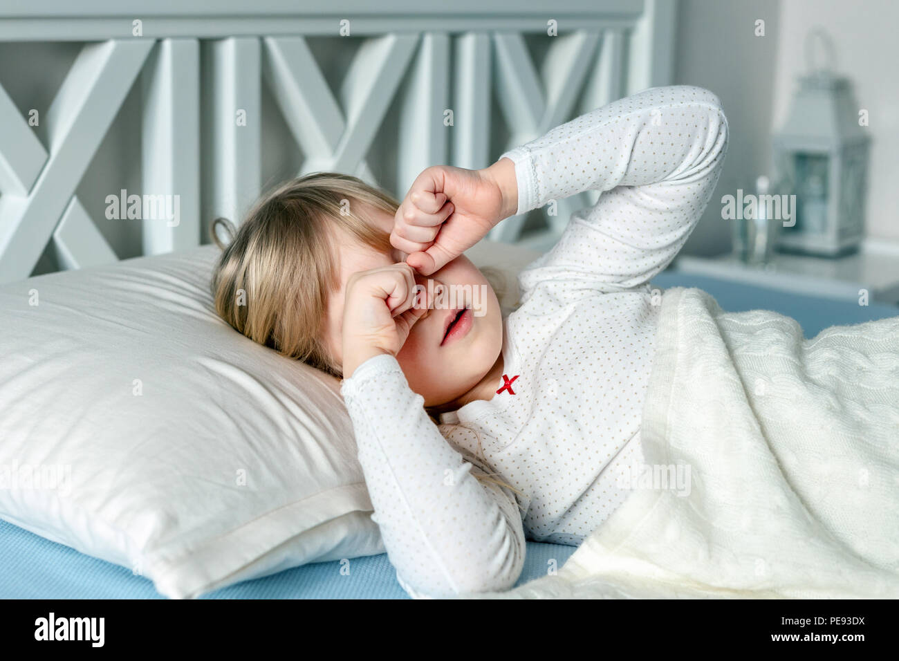 Cute little blond caucasian girl awakening at bed in morning. Child wake up early to go to school. Stretching and yawning. Healthy sleeping. Children  Stock Photo