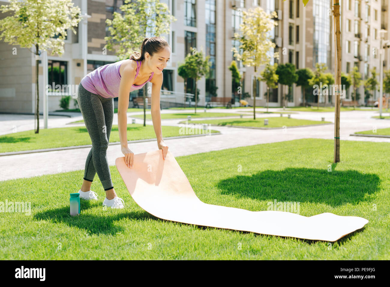 Positive Fit Woman Putting A Yoga Mat On The Grass Stock Photo