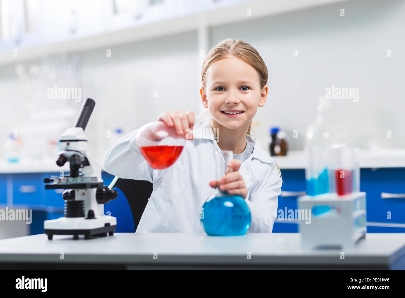 My experiment. Attractive nice cheerful girl using bulbs while posing near microscope and staring at camera Stock Photo