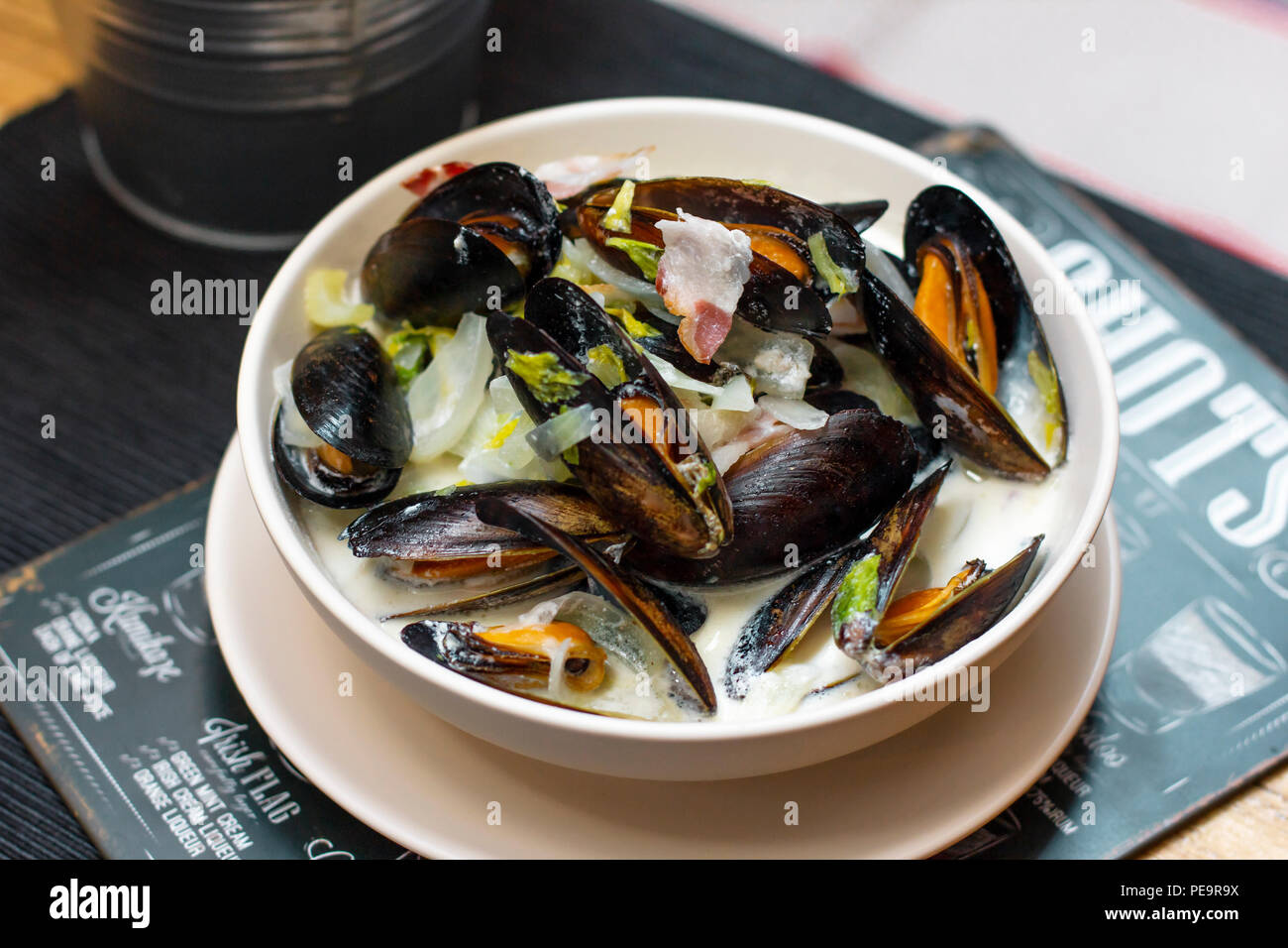 Mussels with onions and bacon in cream sauce in deep plate on the table