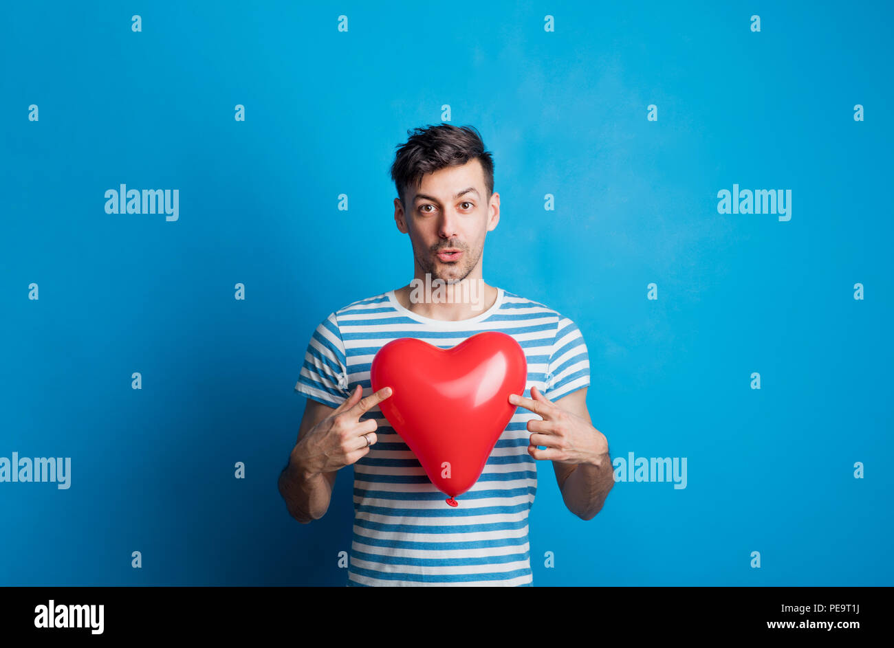 Portrait of a young man in a studio on a blue background, holding red ...
