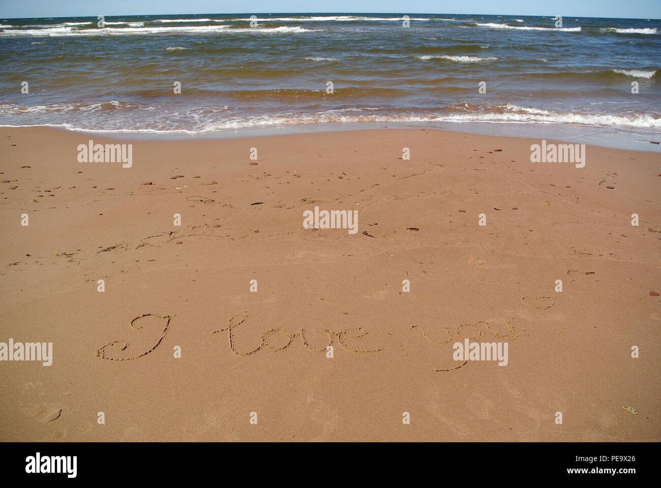 Words 'I love you' beautifully handwritten on red sand on a beach with the sea, sky and waves in the upper part, Prince Edward Island Stock Photo