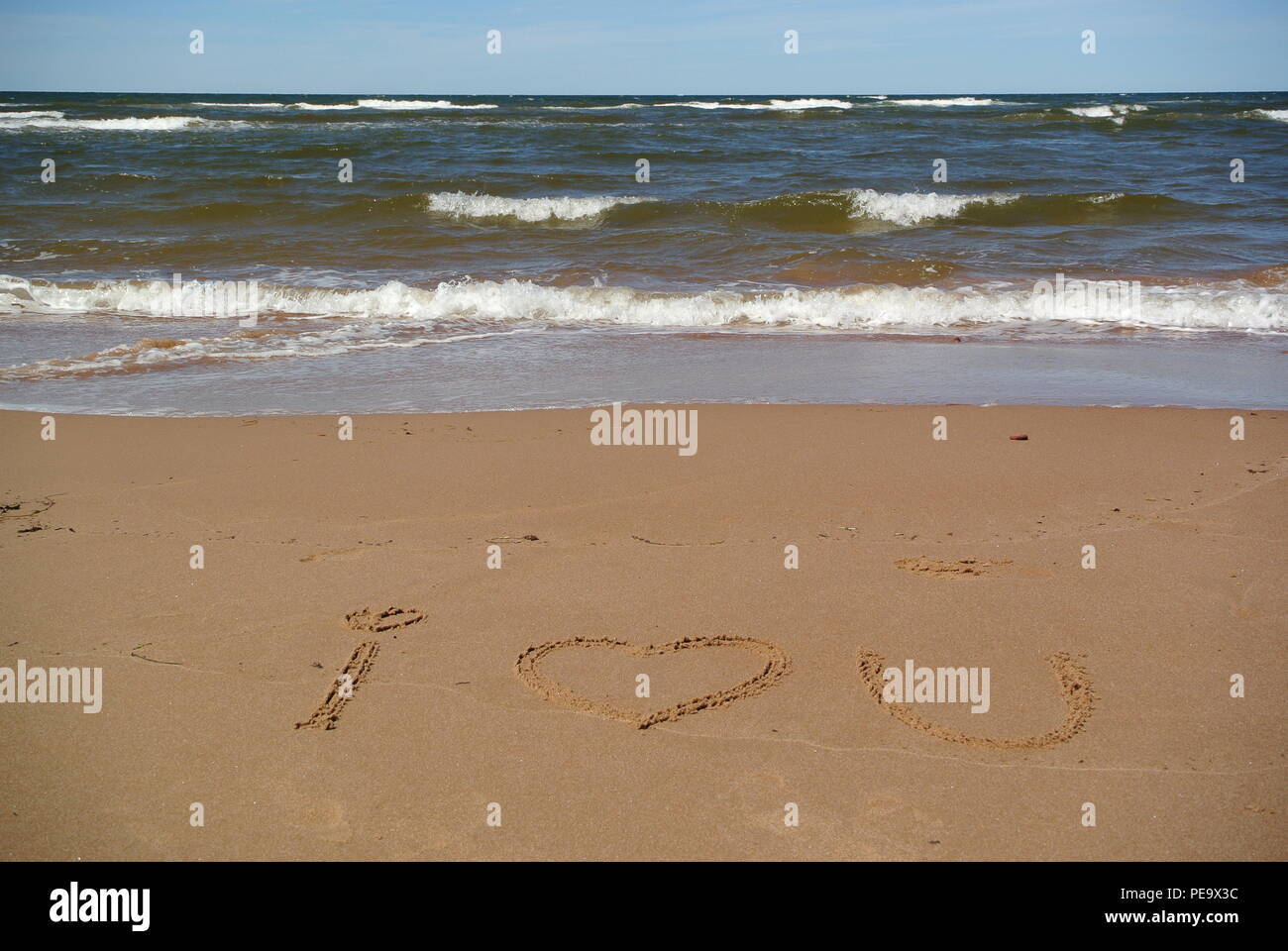 Words 'I love you' (heart symbol) beautifully handwritten on red sand on a beach with the sea, sky and waves in the upper part, Prince Edward Island Stock Photo
