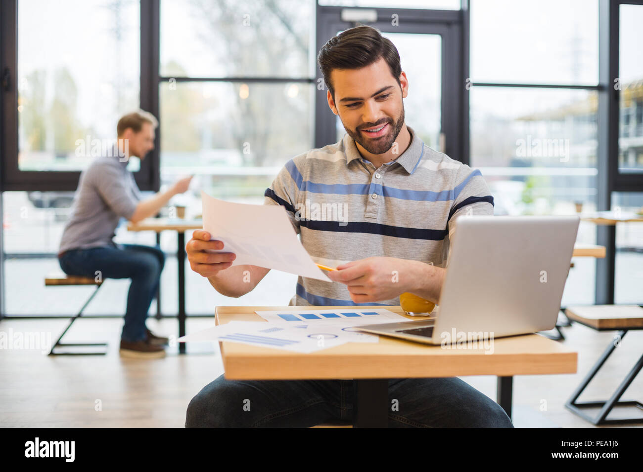 My work. Pleasant delighted nice man sitting at the table and holding a  drawing while looking at the tablet screen Stock Photo - Alamy