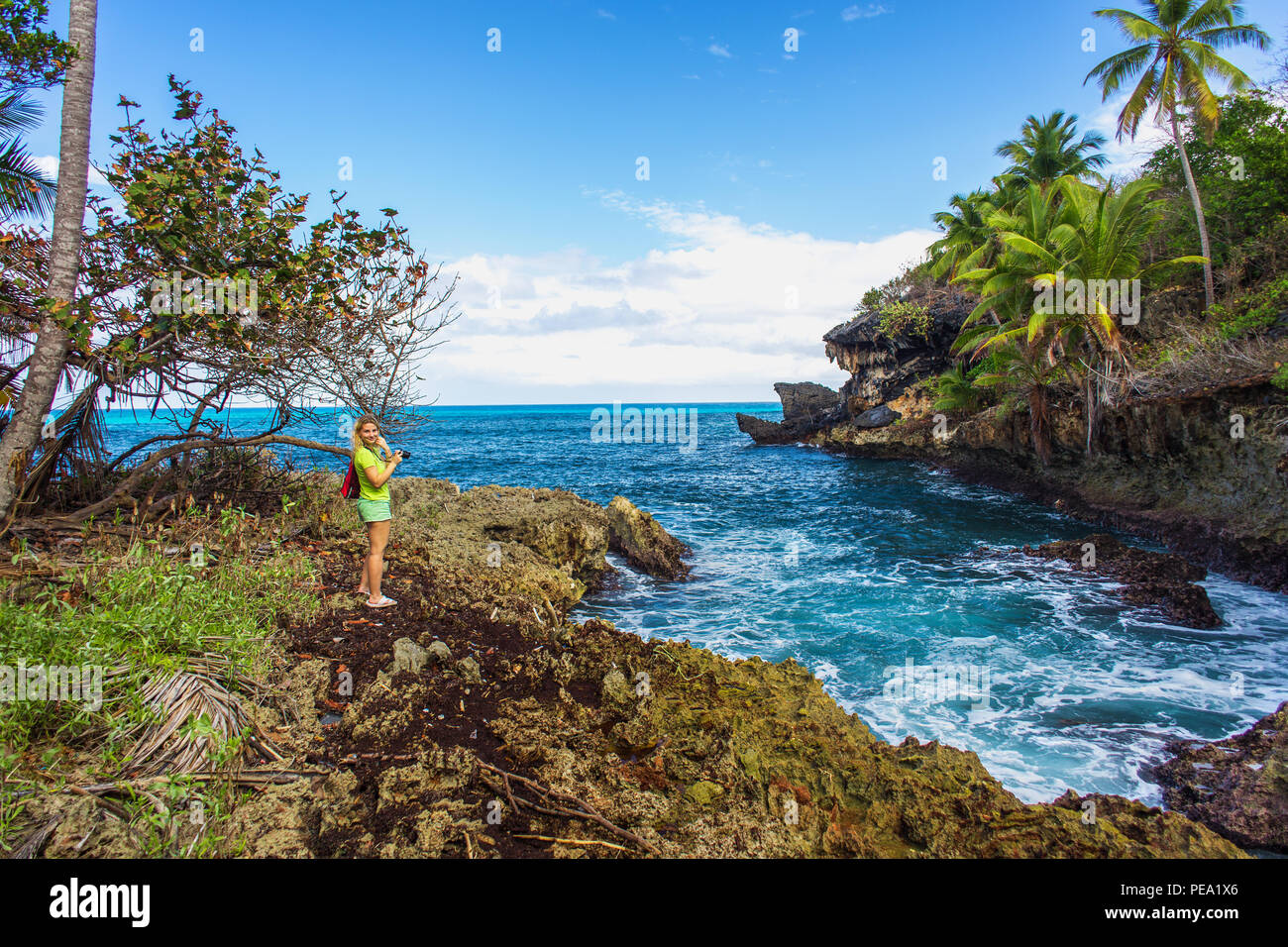 Wild tropical rocky shore, bay, lagoon. Green palm trees on the rocks and girl on the rocks. Las Galeras, Samana, Dominican Republic Stock Photo