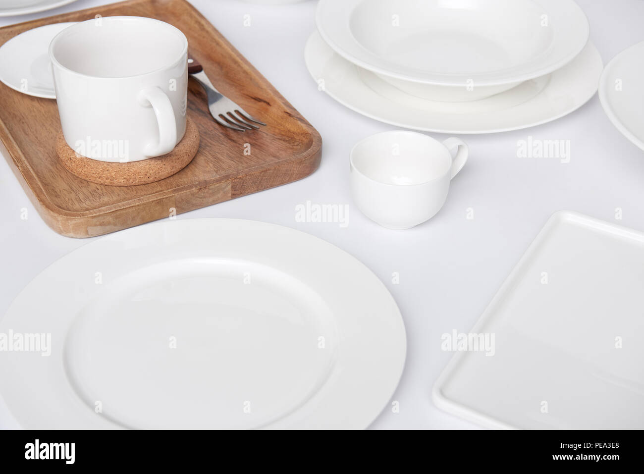 close up view of wooden tray, fork with various plates and cup with bowl on white table Stock Photo