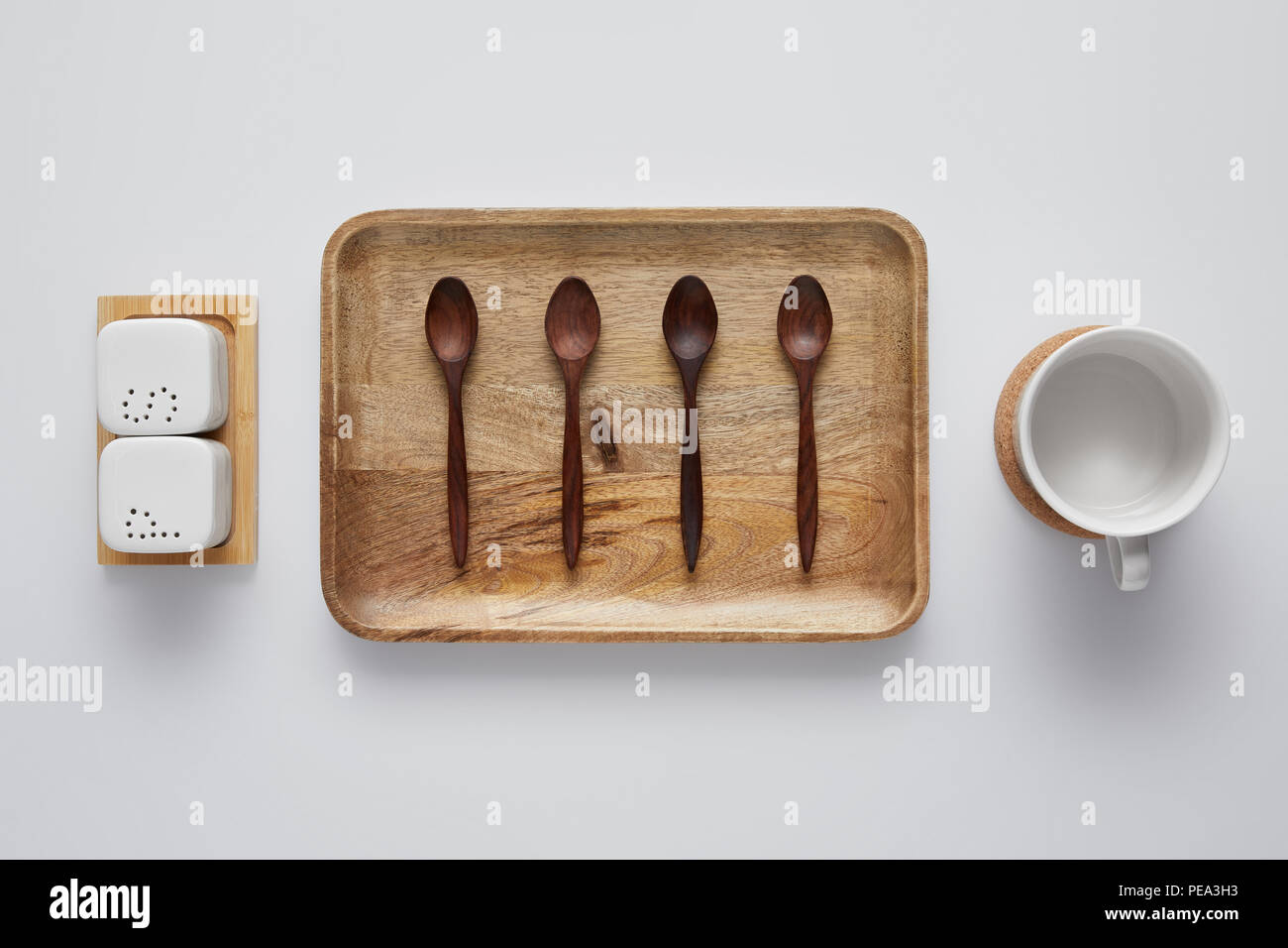 top view of arranged wooden tray with spoons, saltcellar, pepper caster and cup on white table Stock Photo