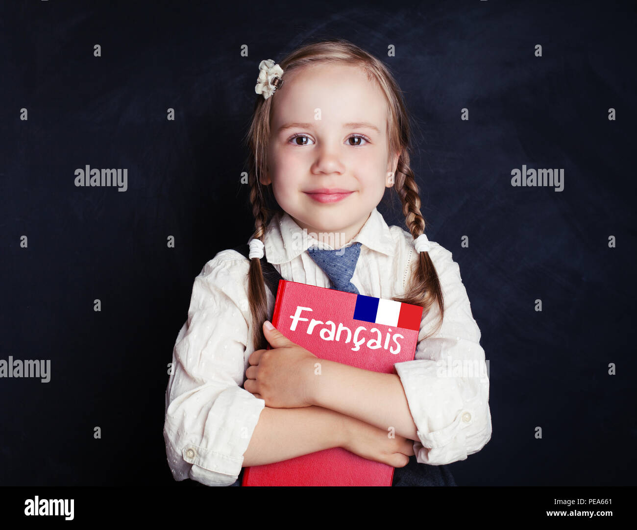 Happy child girl pupil with French study book against language school chalkboard. Learning French concept Stock Photo