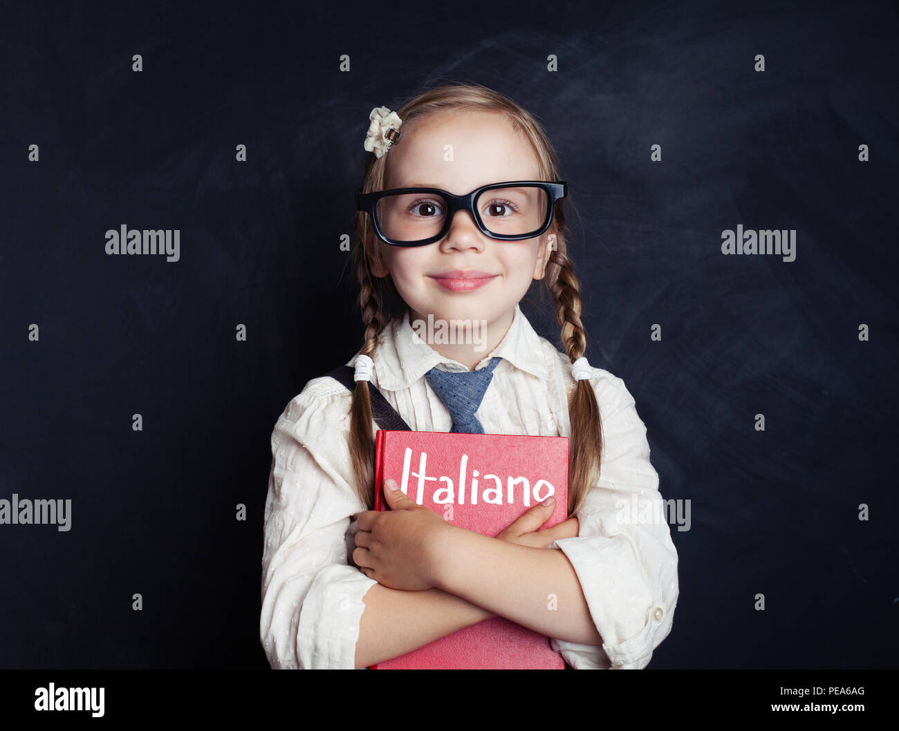 Happy little child girl hugging italian book against chalkboard background in school classroom. Learning italian and education concept Stock Photo