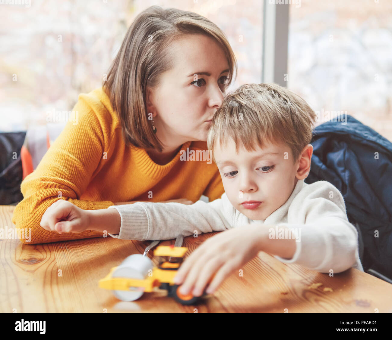 Portrait of white Caucasian happy family, mother and son, sitting in restaurant cafe at table, kissing playing with toy car, authentic lifestyle Stock Photo