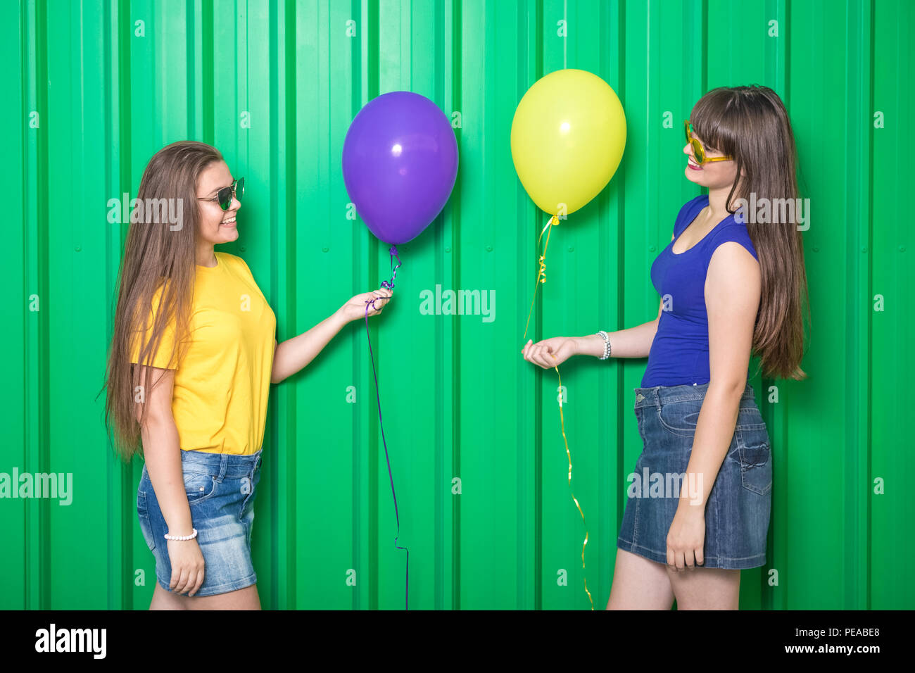 Two friends with balloons against green background Stock Photo - Alamy