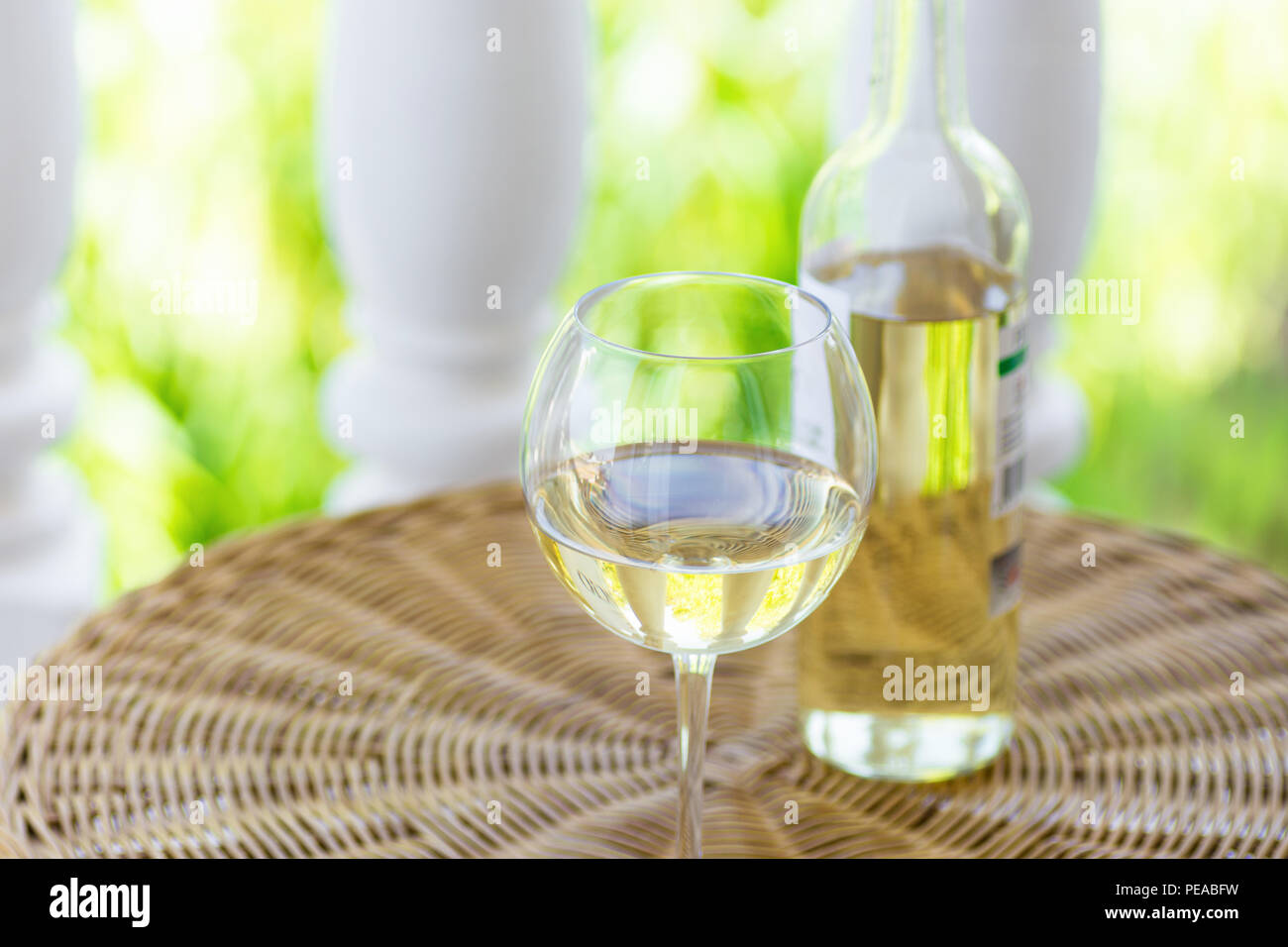 Glass of white dry wine and bottle on wicker table on garden terrace of villa or mansion. Authentic lifestyle image. Relaxation indulgence gourmet. Po Stock Photo