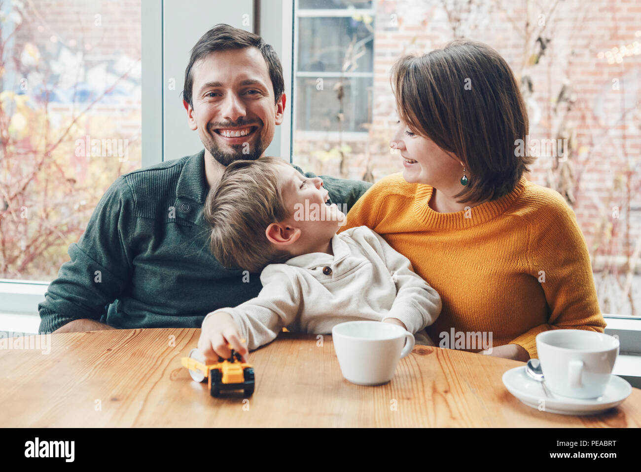 Portrait of white Caucasian happy family of three mother, father and son, sitting in restaurant cafe at table, smiling playing, authentic lifestyle Stock Photo