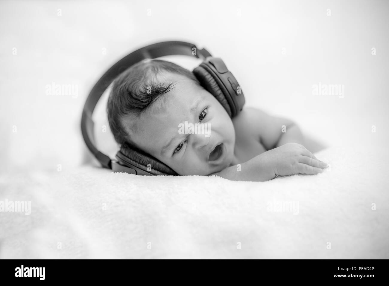 Cute newborn baby hearing music with headphones on a blanket - happy family moments Stock Photo