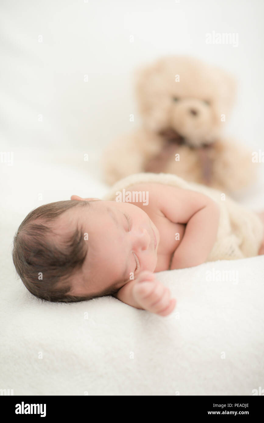 Cute newborn baby sleeps on a blanket with a toy teddy bear happy