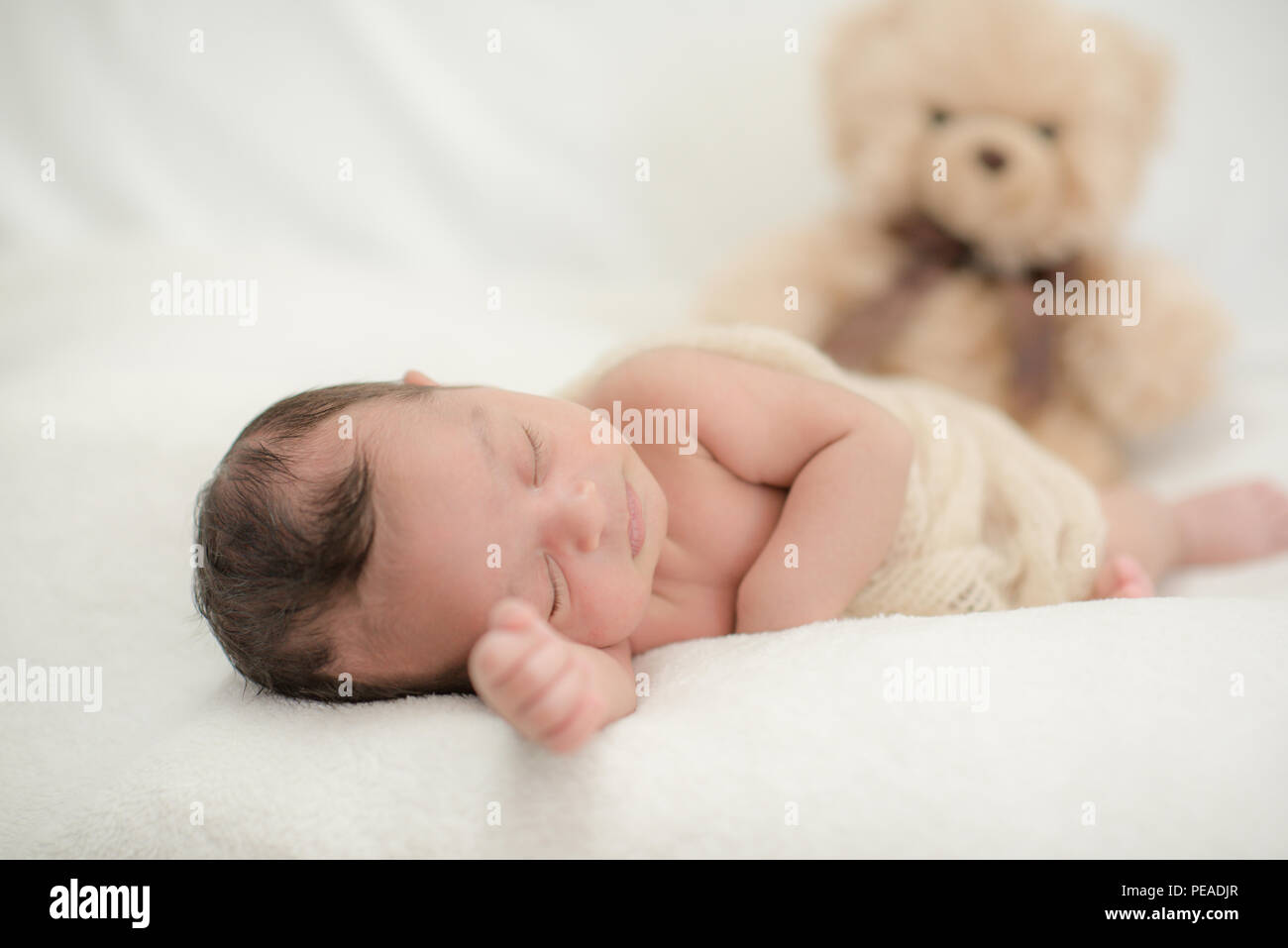 Cute newborn baby sleeps on a blanket with a toy teddy bear happy