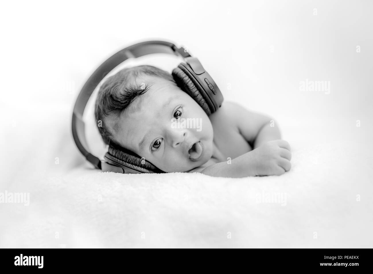 Cute newborn baby hearing music with headphones on a blanket - happy family moments Stock Photo