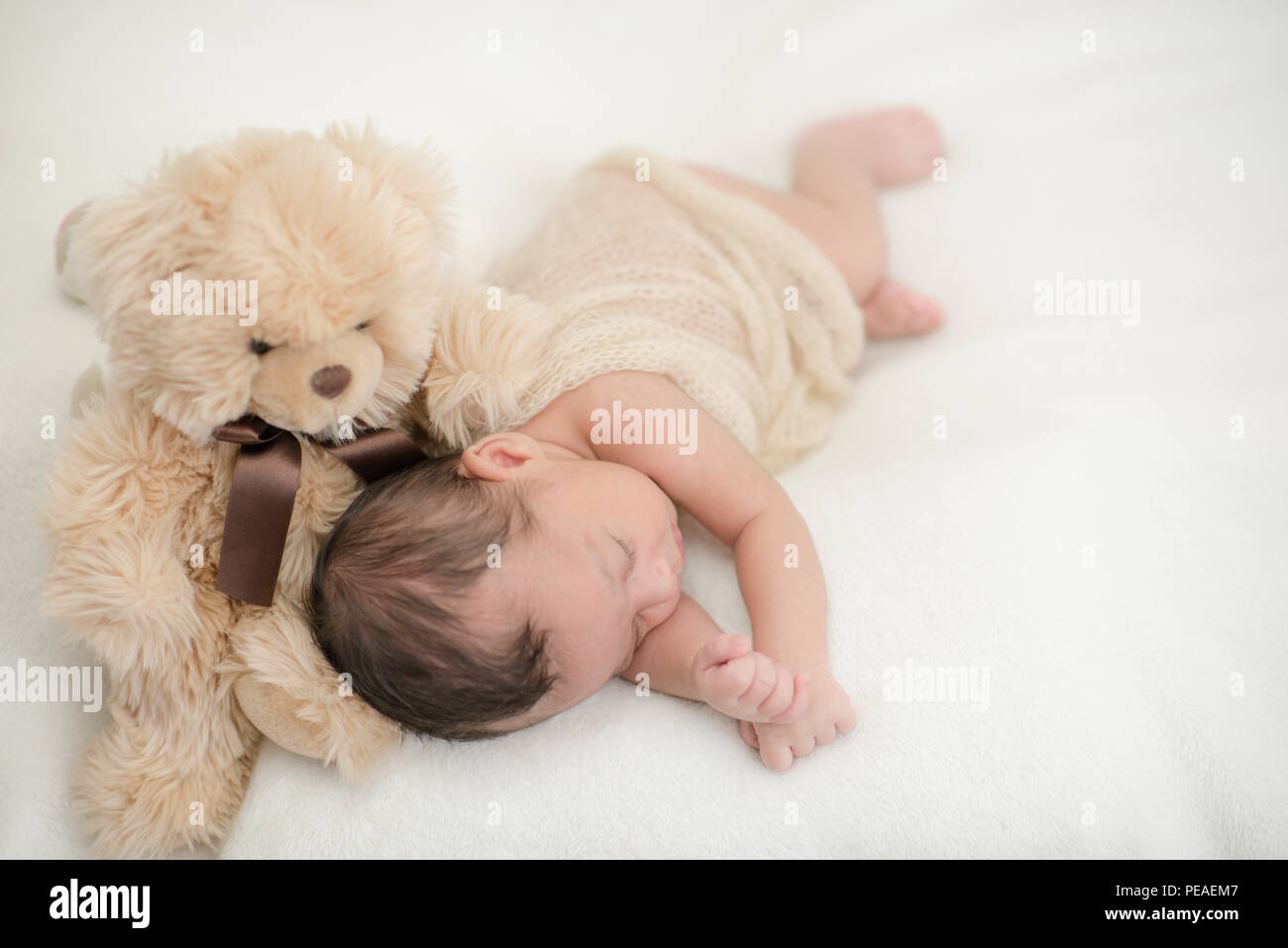 Cute newborn baby sleeps on a blanket with a toy teddy bear happy