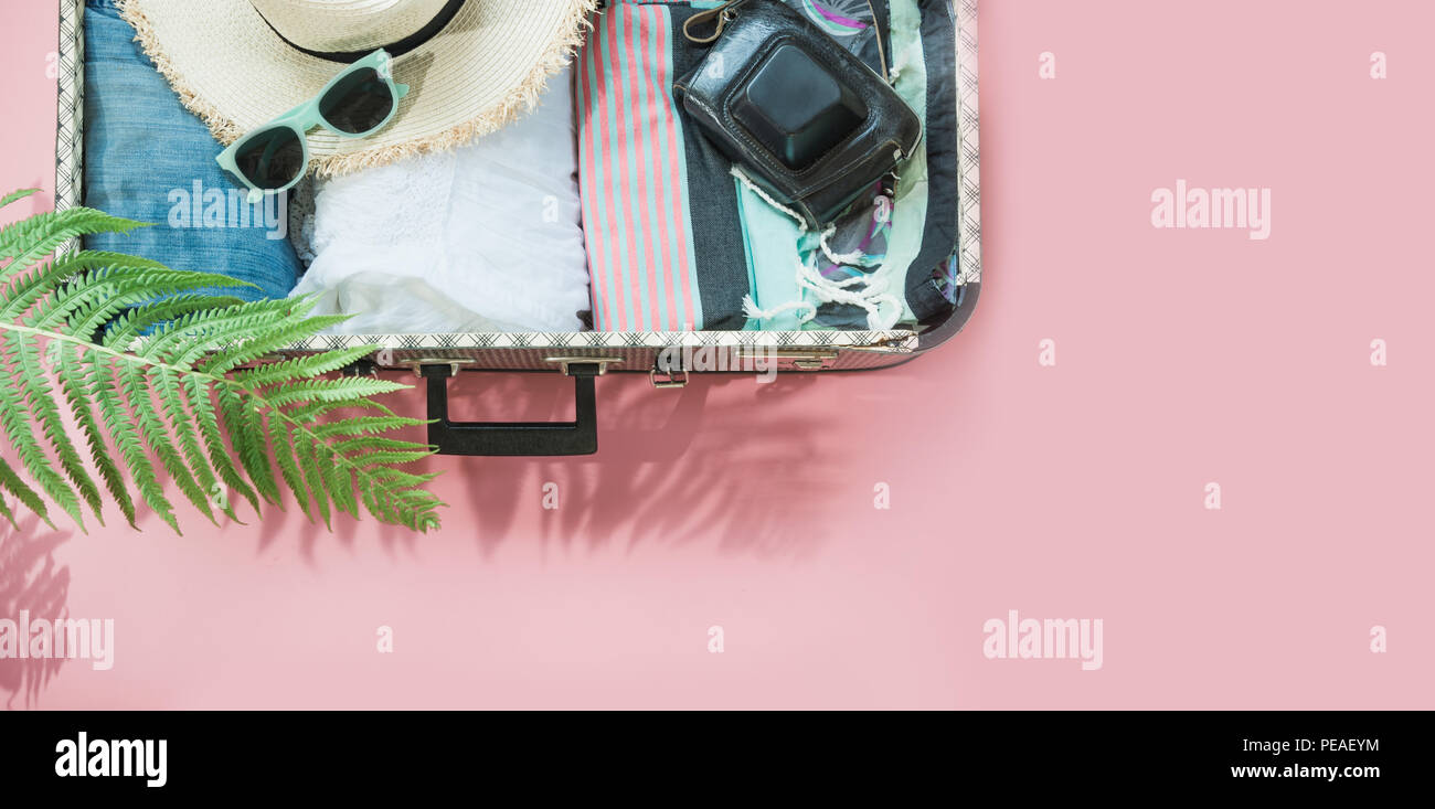 Open suitcase with female clothes for trip on pastel pink. Top view with copy space. Summer concept travel. Stock Photo