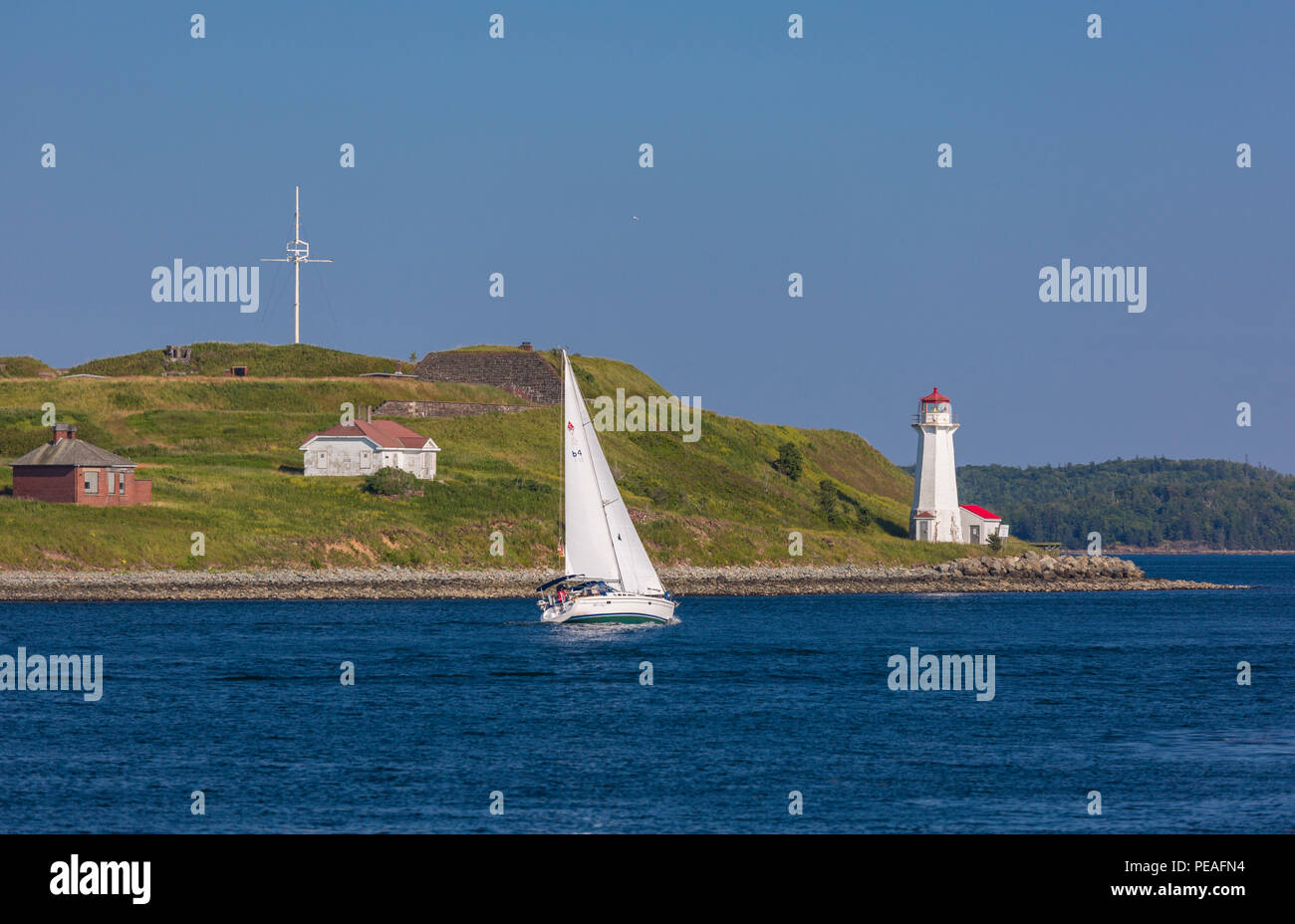 HALIFAX, NOVA SCOTIA, CANADA - Sailboat passes lighthouse on McNabs Island in Halifax seaport harbor. Stock Photo