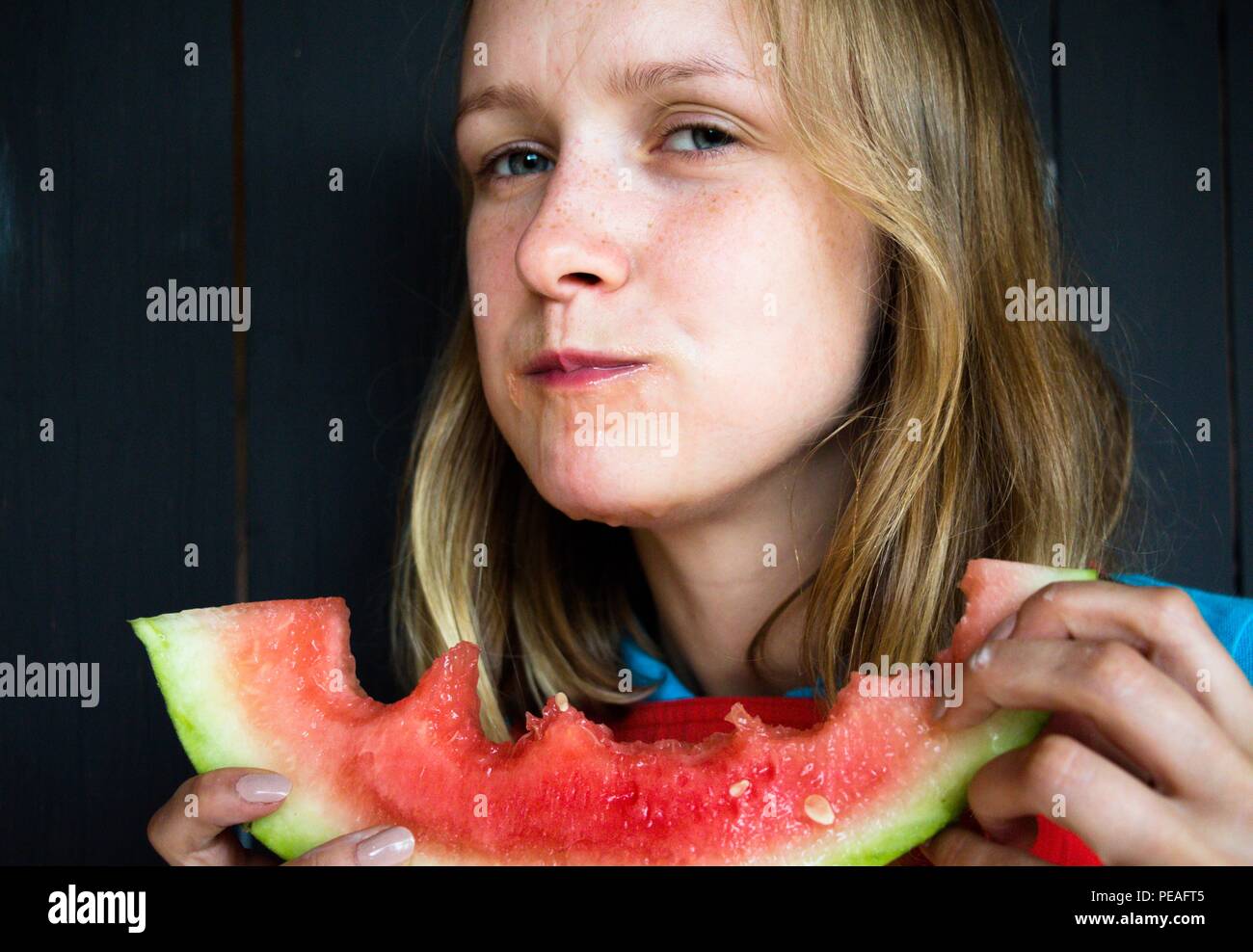 A beautiful and young girl eats a juicy watermelon. The juice drips down her chin. Watermelon is very tasty and it enjoys its taste. Stock Photo