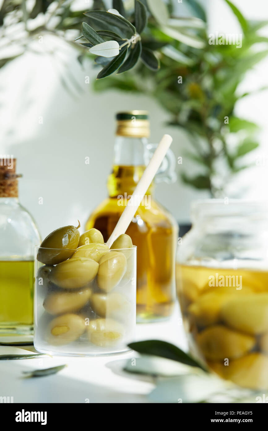 glass with spoon and green olives, jar, various bottles of aromatic