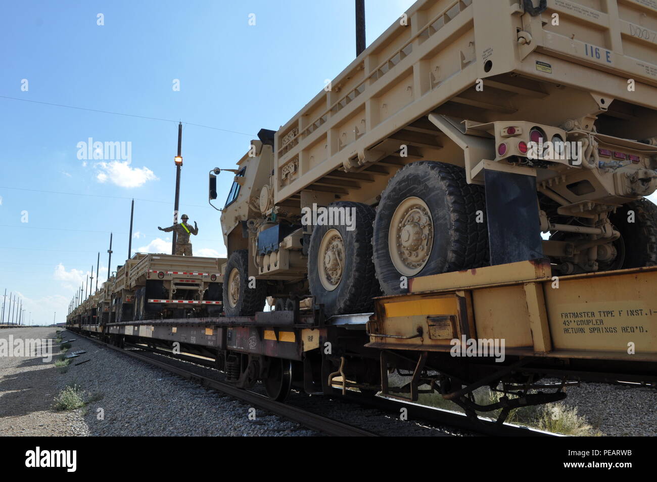 Sgt. Ben Davis, standing atop railcar, allied trade specialist, 682nd Engineer Battalion, guides the driver of the five-ton dump truck as it is being loaded onto flatcars for shipment. The spanner can be seen between the two rear wheels, connecting the two flatcars allowing the equipment to advance. The loading process for all heavy machinery is a three man job, with a ground guide in front to guide the machine, the driver or heavy machine operator who operates the equipment and a ground spotter, who ensures the spanners are in place so that the machine can move across the gaps between flatcar Stock Photo
