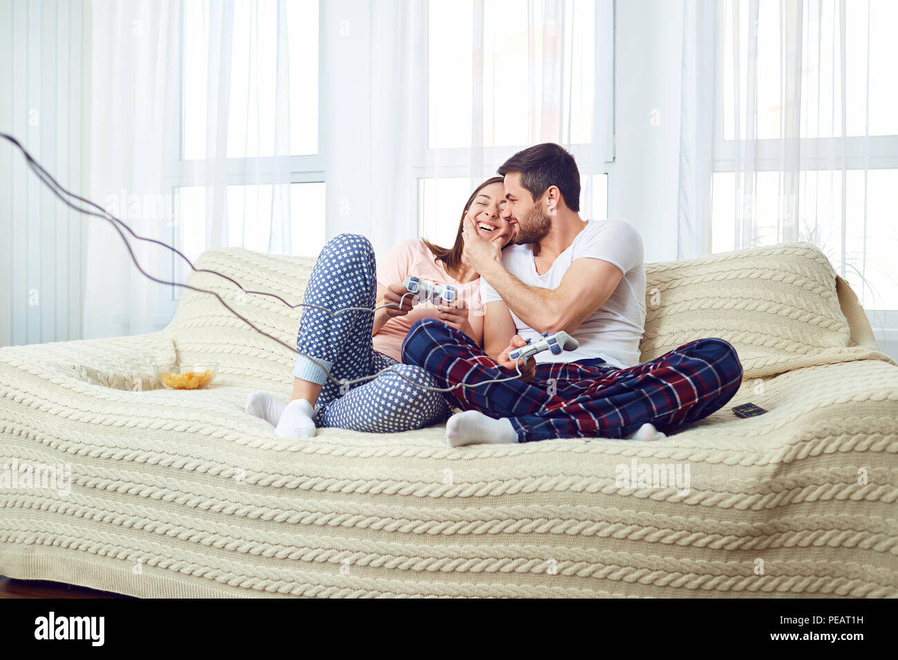 Couple playing video game sitting on sofa in room. Stock Photo