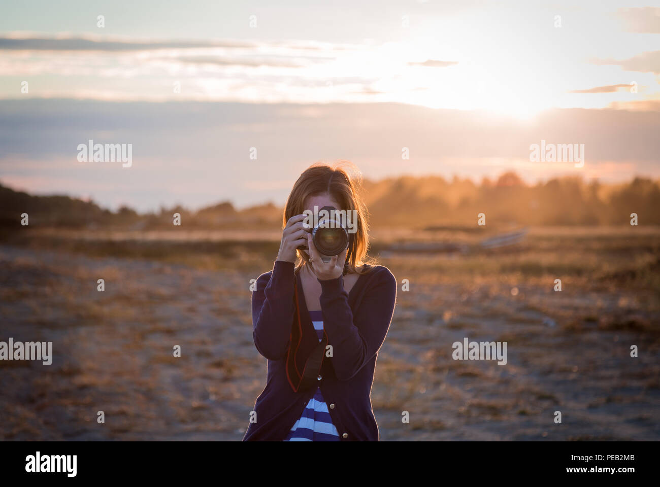 A girl taking a photo with a DSLR with the sunset in the background. Stock Photo