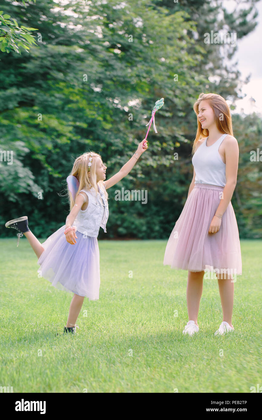 Portrait of two smiling funny Caucasian girls sisters wearing pink tutu tulle skirts in park forest meadow at sunset. Friends having fun together. Gir Stock Photo