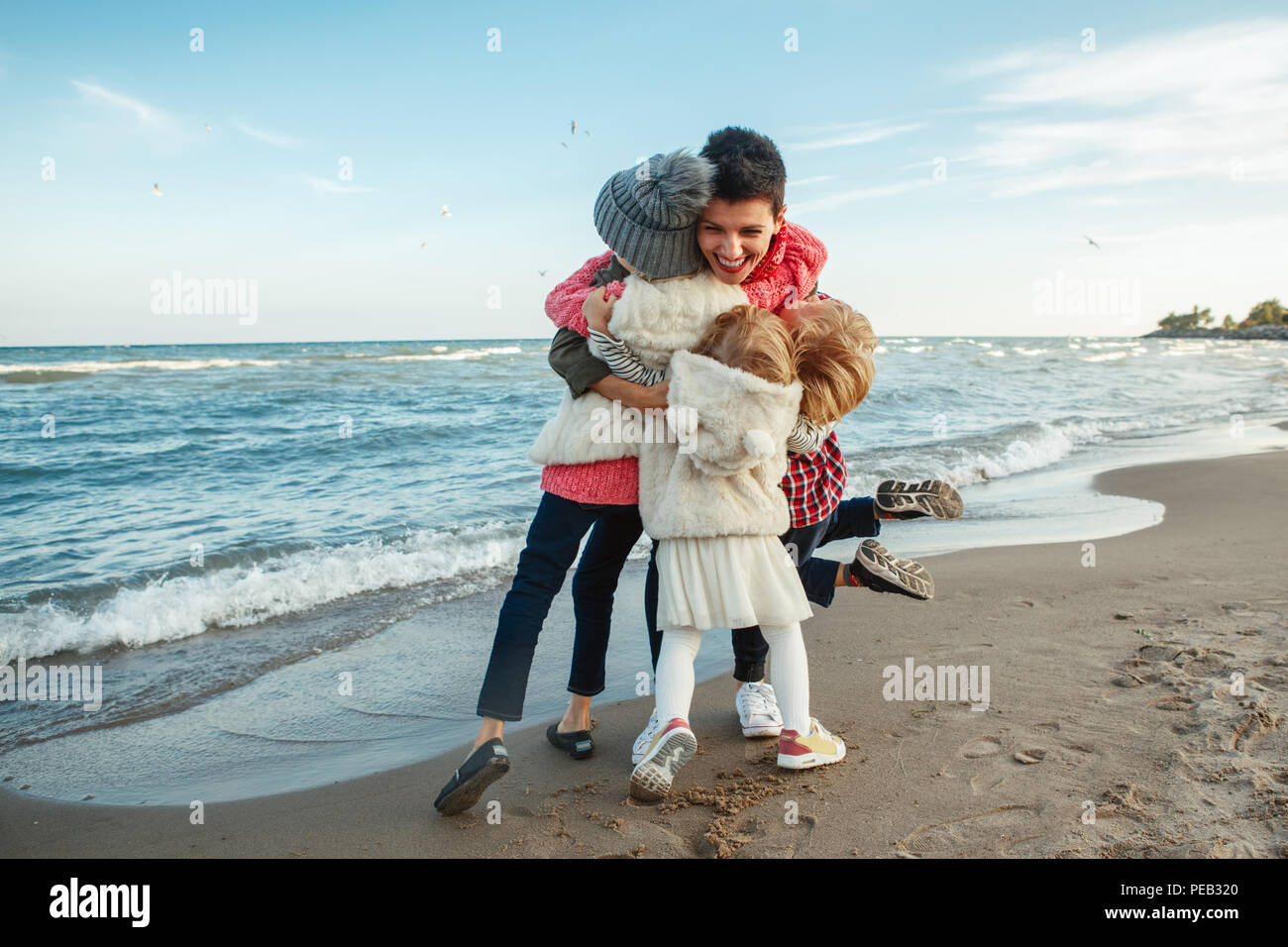 Group portrait of white Caucasian family, mother with three children kids hugging smiling laughing on ocean sea beach on sunset outdoors, happy lifest Stock Photo