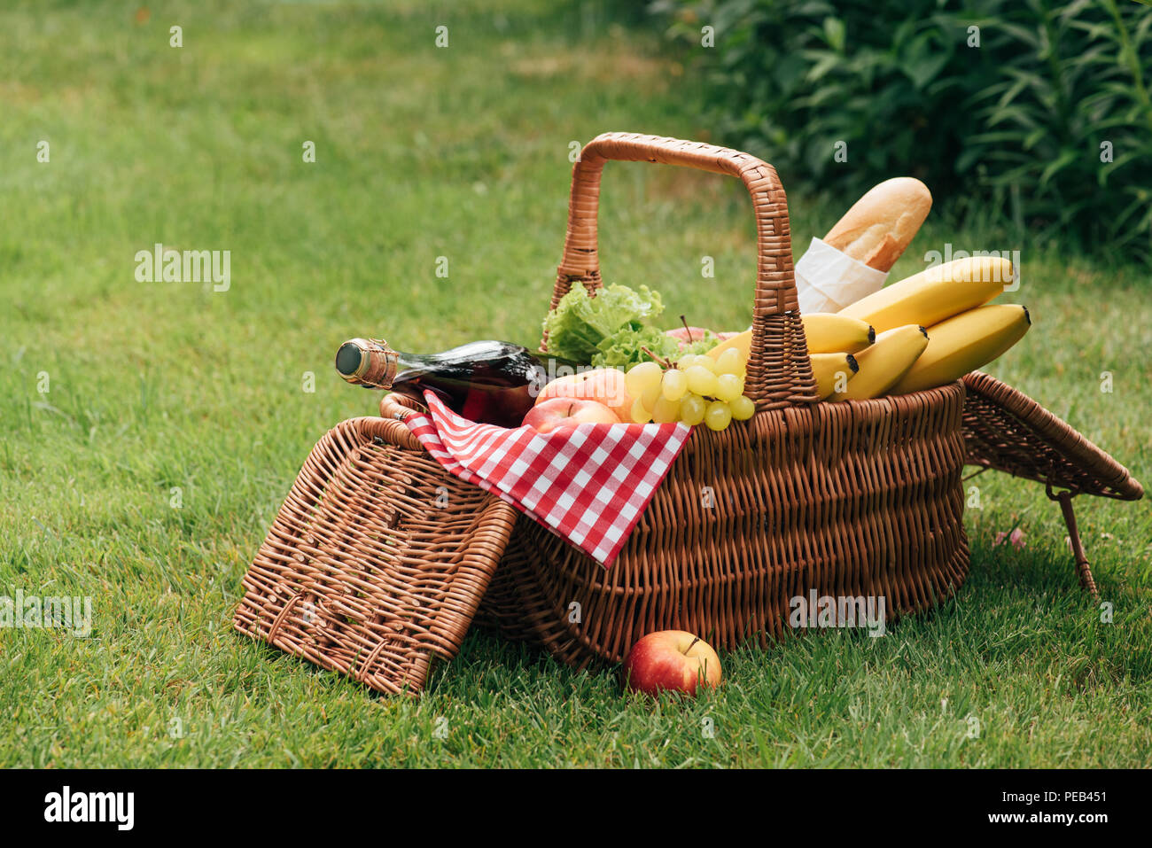 tasty fruits and bottle of champagne in wicker basket on green grass at picnic Stock Photo