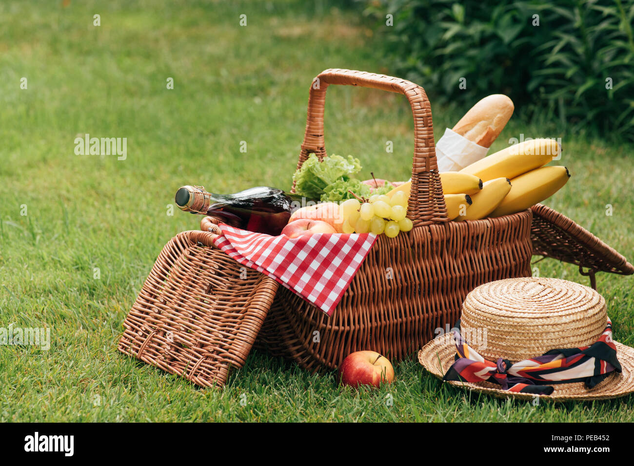 yummy fruits and bottle of champagne in wicker basket on green grass at picnic Stock Photo