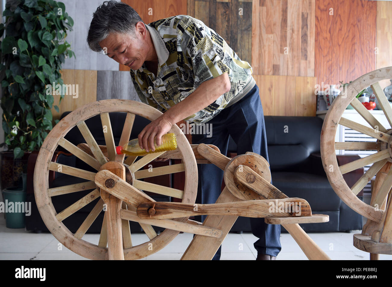 Pingliang, China's Gansu Province. 14th Aug, 2018. He Yong lubricates the bearing of a wooden bicycle in Liuhu Township of Pingliang City, northwest China's Gansu Province, Aug. 14, 2018. The 55-year-old farmer He Yong successfully made a 1.8-meter-long and 0.98-meter-high wooden bicycle in 2017. The bike was made purely of wood, including walnut and elm. Credit: Fan Peishen/Xinhua/Alamy Live News Stock Photo